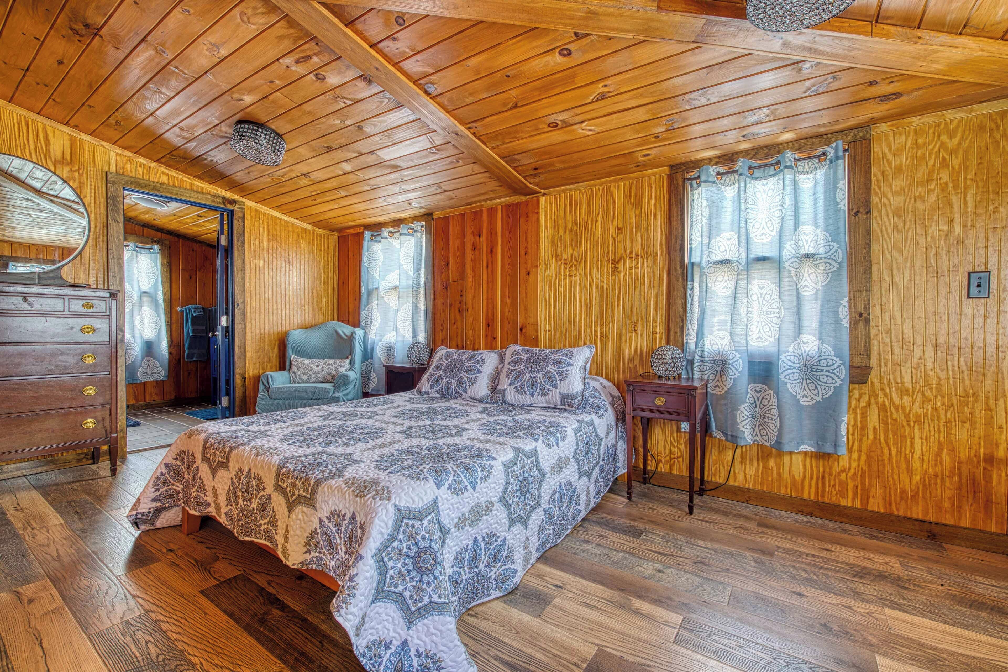 Une chambre aux murs lambrissés, avec un grand lit, une commode, une chaise et une table de chevet.