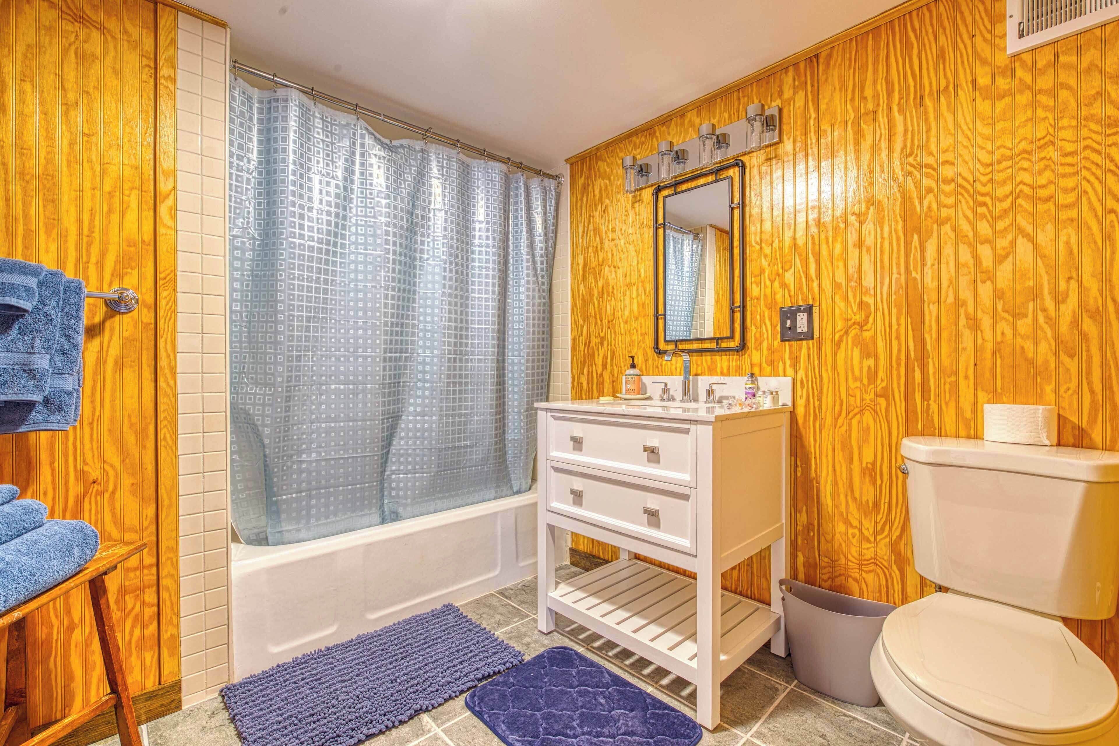 A bathroom with wooden paneling, a white vanity with a mirror, a bathtub, and a toilet.