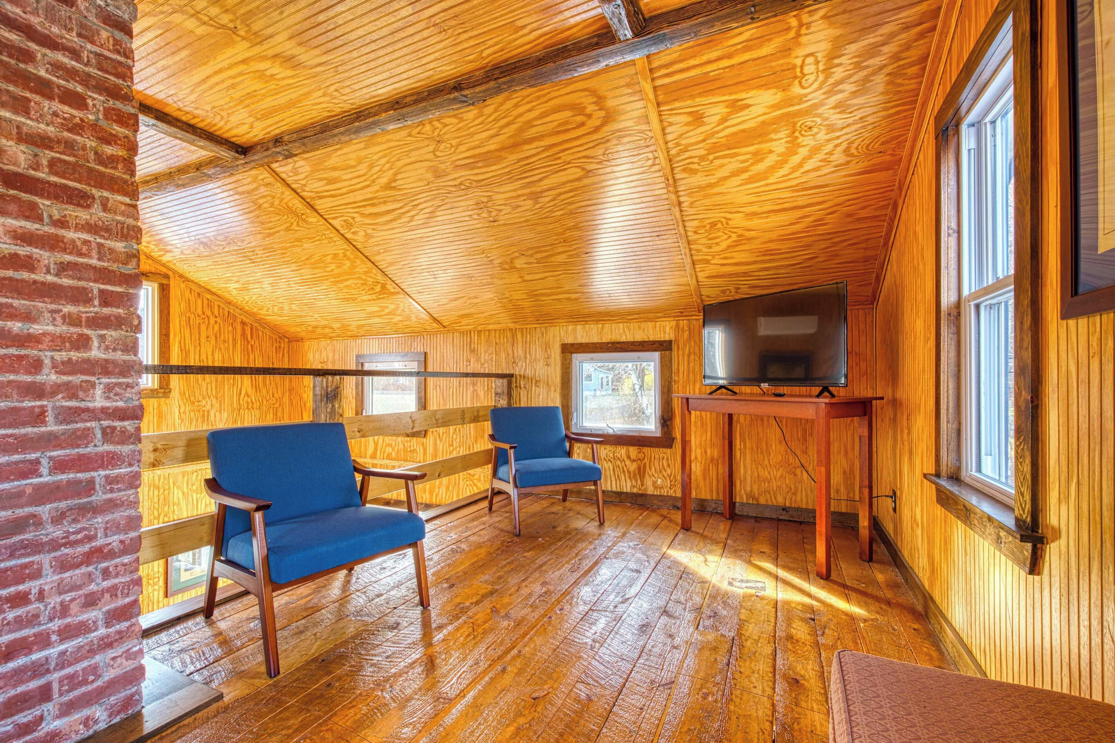 A cozy cabin with wooden walls and floors, two blue chairs, a television on a wooden table, and a brick wall.