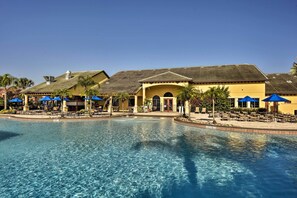 A pool area with lounge chairs and umbrellas, a building with a tiled roof, and palm trees. - Grou-friendly Kissimmee Home: 7 Mi to Disney Parks (Kissimmee)