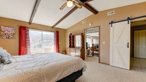 A bedroom with a large bed, a ceiling fan, a sliding barn door, and a view of a balcony.