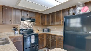 A kitchen with wooden cabinets, a black refrigerator, a microwave, and a stove.