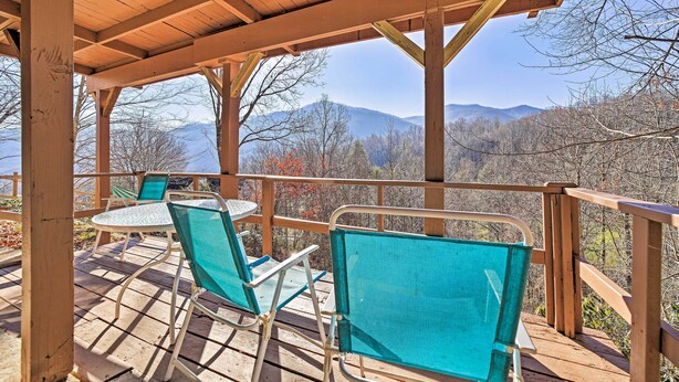 A wooden deck with two chairs and a table, overlooking a mountainous landscape.