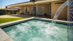 Ein Pool mit Wasserspiel, eine überdachte Terrasse mit Sitzgelegenheiten und ein Gebäude mit einem Ziegeldach.