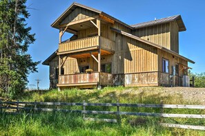 A two-story wooden cabin with a balcony, surrounded by a wooden fence and lush greenery.
