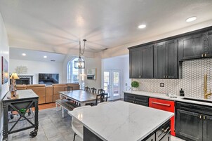 A modern kitchen with dark cabinets, a marble island, and a dining area with a sofa and TV.