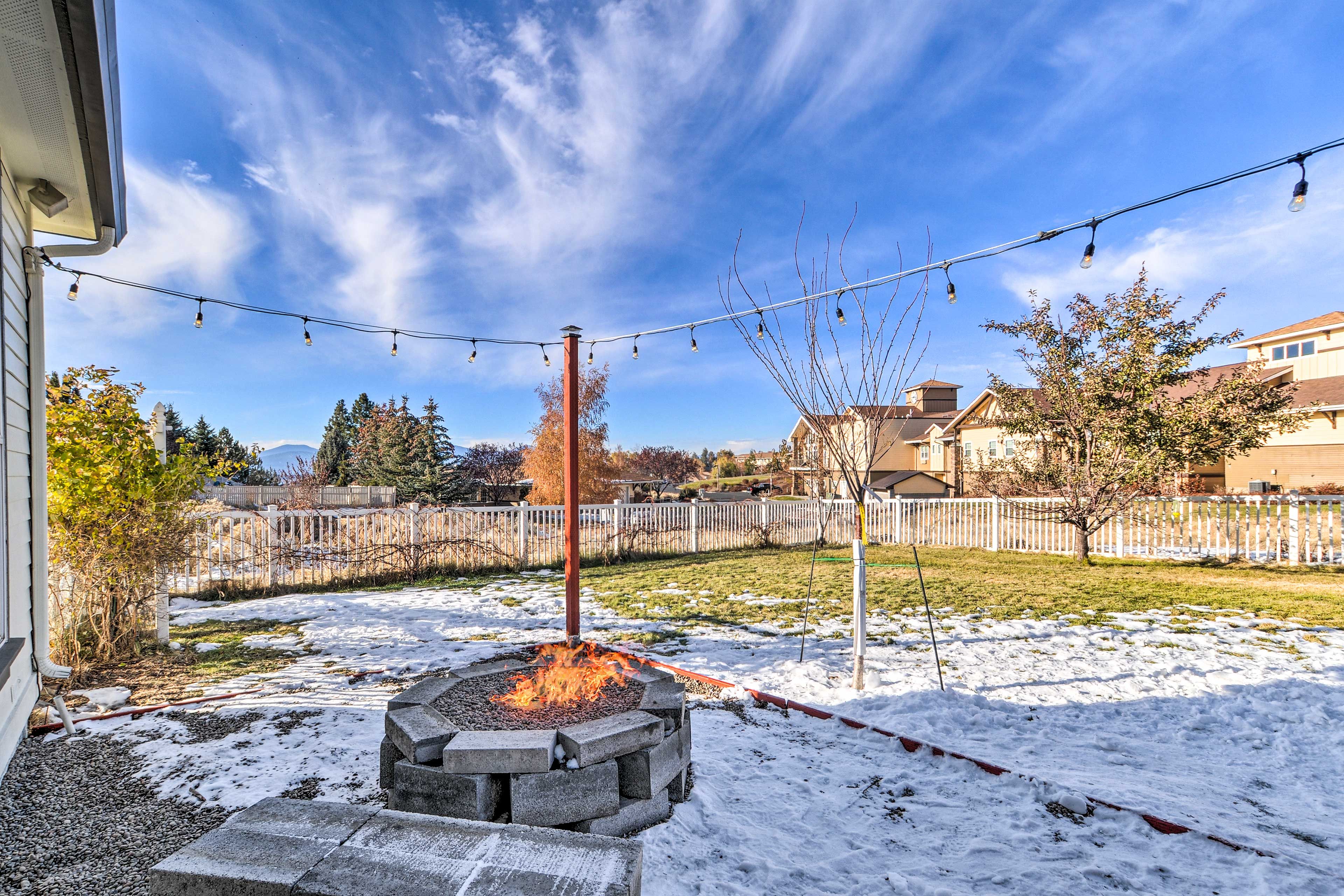 A backyard with a fire pit, string lights, and a snow-covered lawn.