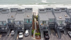 Un complejo de apartamentos frente al mar, con varios balcones, un paseo central y espacios de estacionamiento.