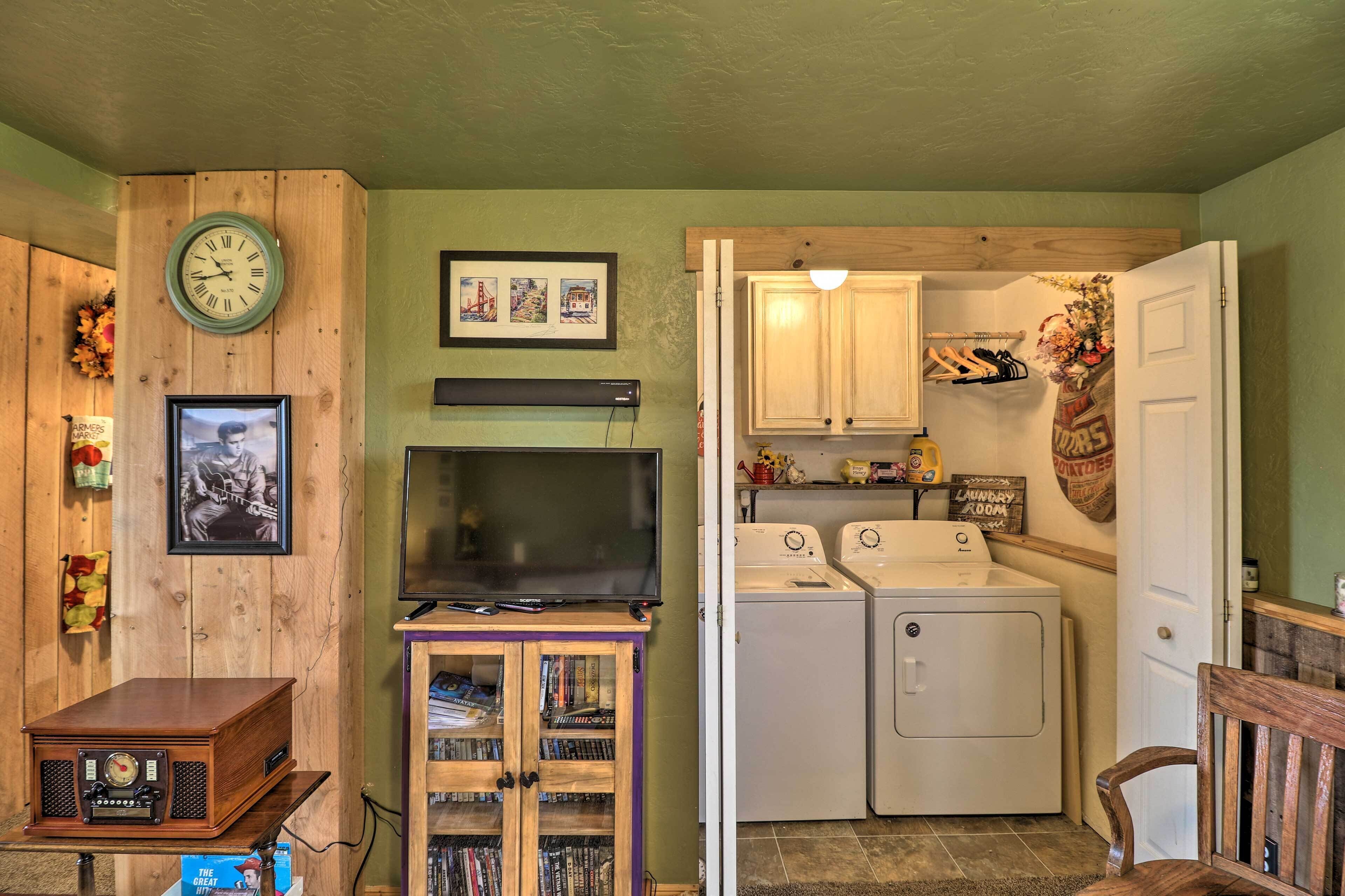 A laundry room with a washing machine and dryer, a clock on the wall, and a television on a stand.