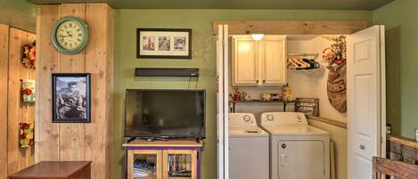 A laundry room with a washing machine and dryer, a clock on the wall, and a television on a stand.