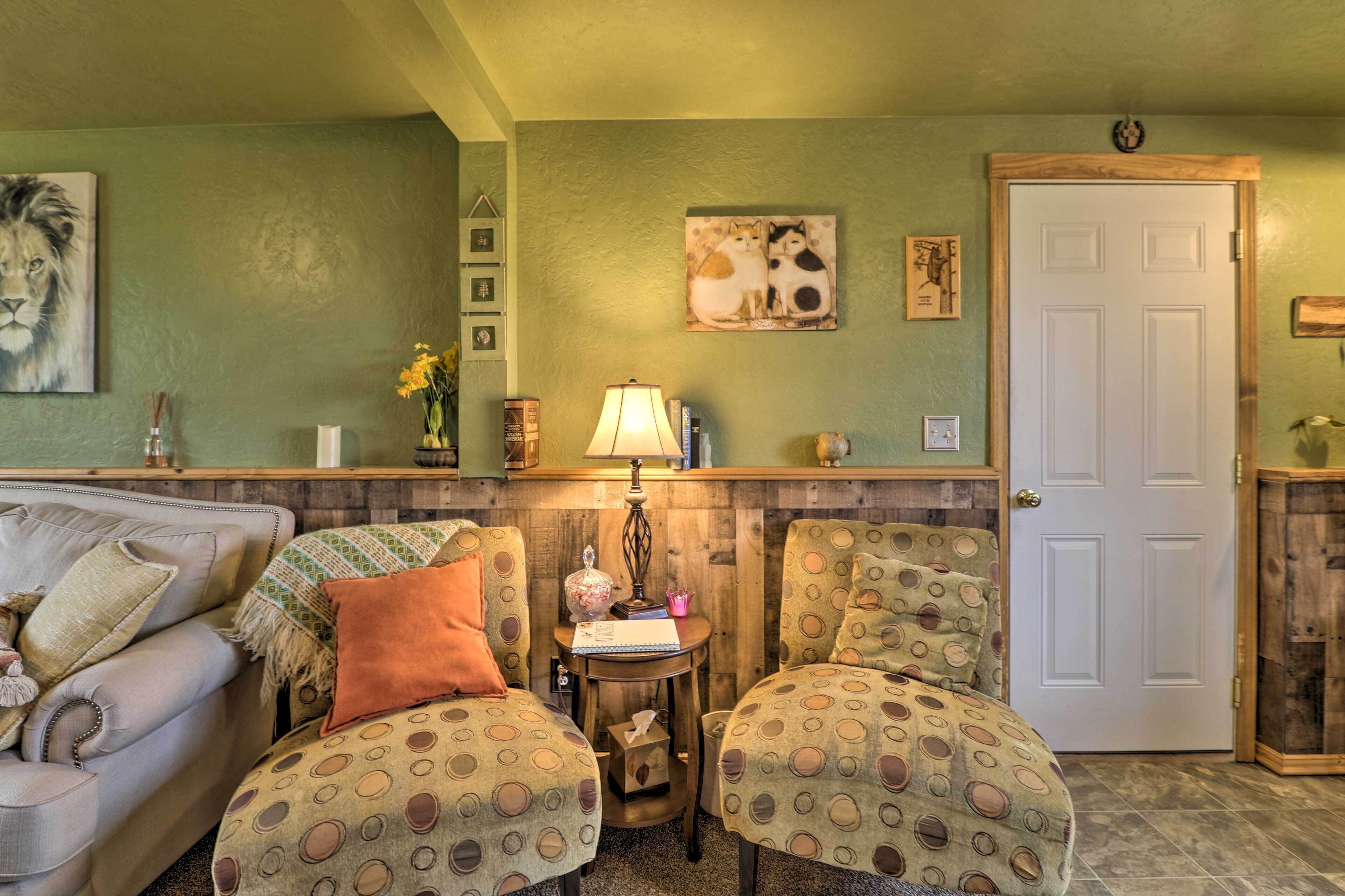 A cozy living room with a sofa, two patterned armchairs, a small table with a lamp, and a door.