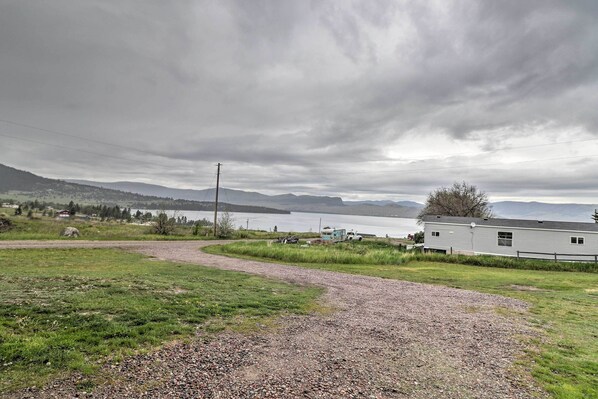 A gravel path leading to a building near a lake, surrounded by grassy fields and mountains.