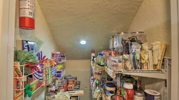 A narrow, cluttered pantry with shelves stocked with canned goods, jars, and various food items.