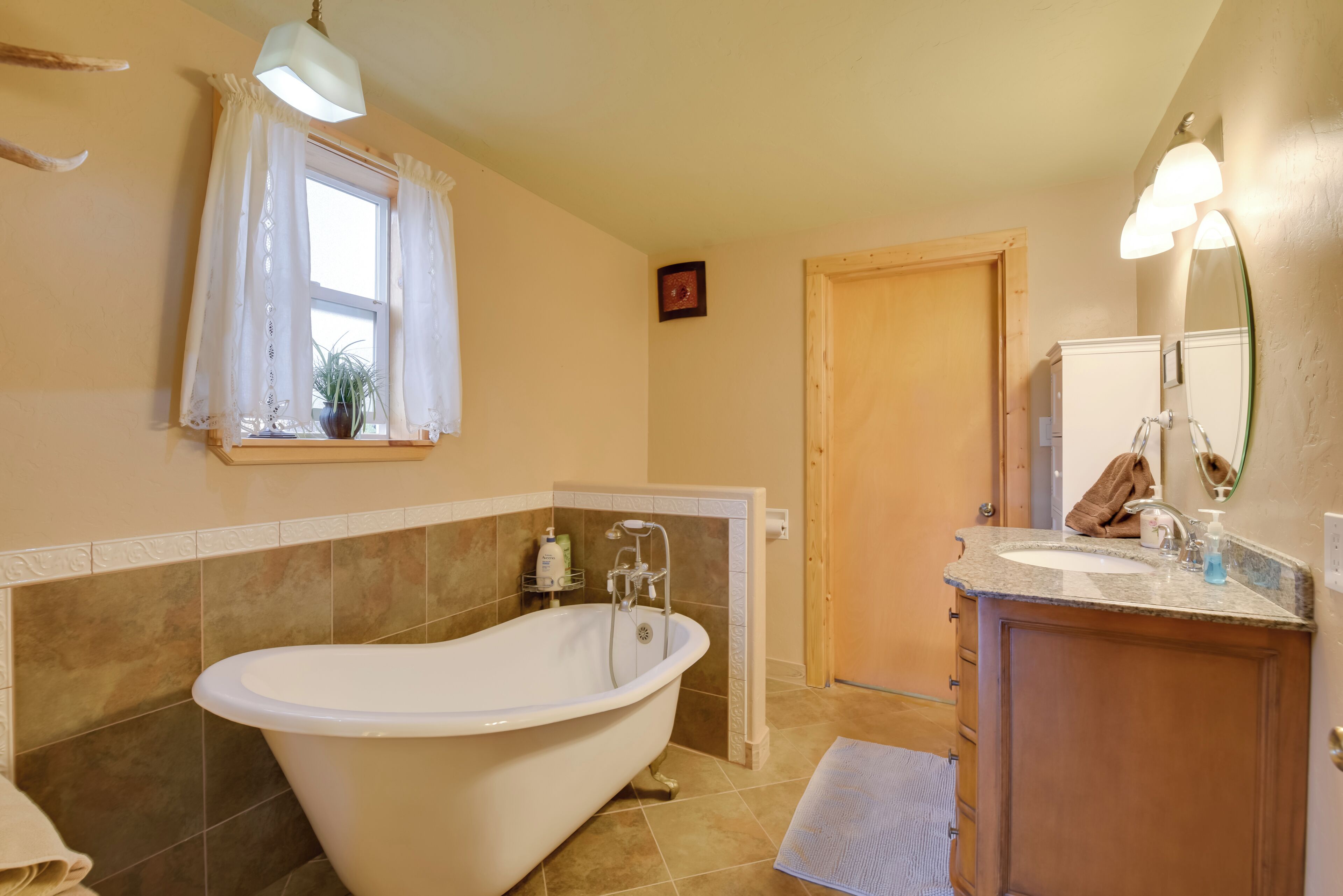 A bathroom with a freestanding bathtub, a vanity with a mirror, and a window with curtains.