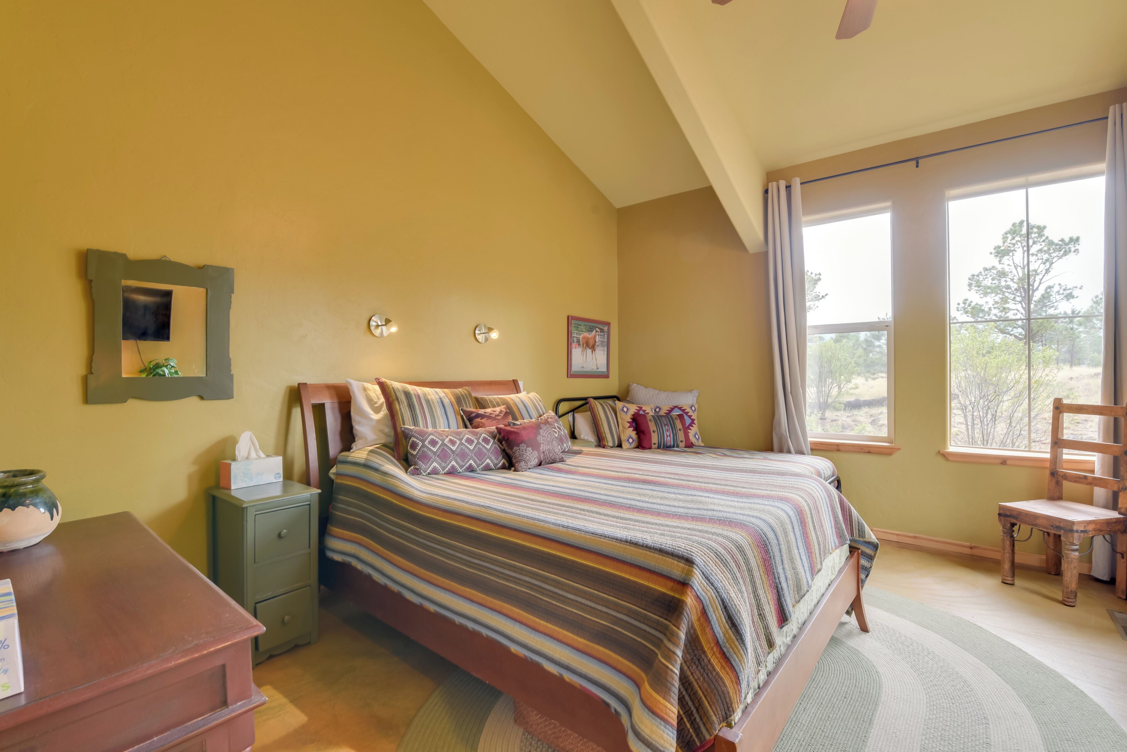 A bedroom with a bed, nightstand, chair, and large windows with a view.