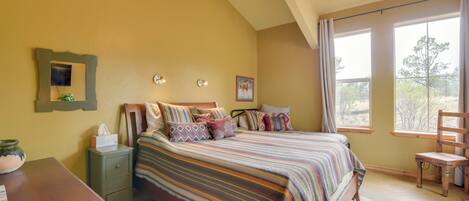 A bedroom with a bed, nightstand, chair, and large windows with a view.