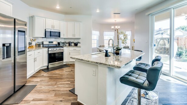 A modern kitchen with white cabinets, stainless steel appliances, a granite countertop, and a bar area with bar stools. - Fresno Home w/ Grill - 9 Mi to Downtown (Fresno)