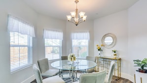 A dining area with a glass table surrounded by chairs, a chandelier, and a console table with decorative items. - Fresno Home w/ Grill - 9 Mi to Downtown (Fresno)