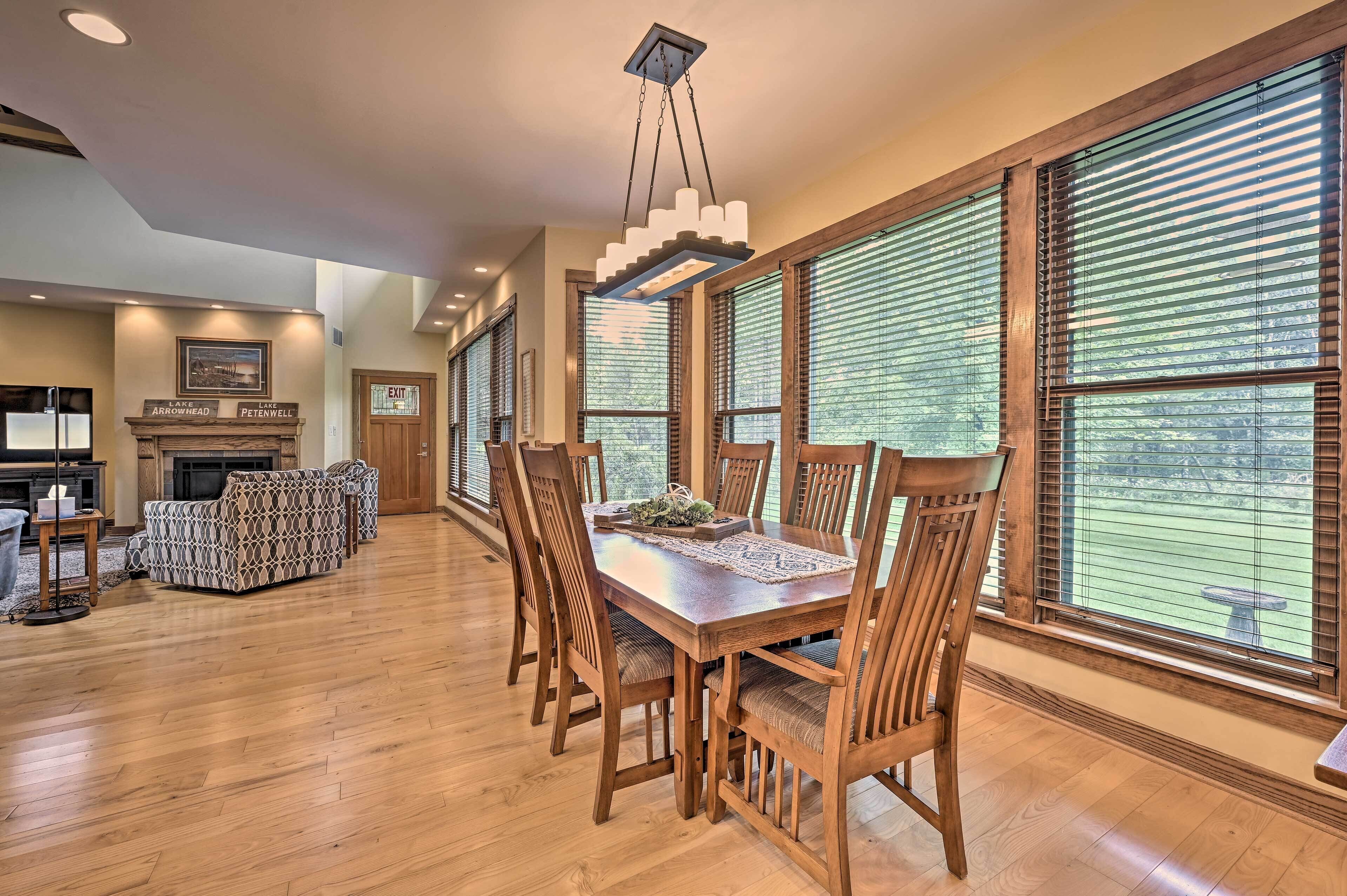 A spacious dining area with a wooden table and chairs, large windows with blinds, a fireplace, and a view of the outdoors.