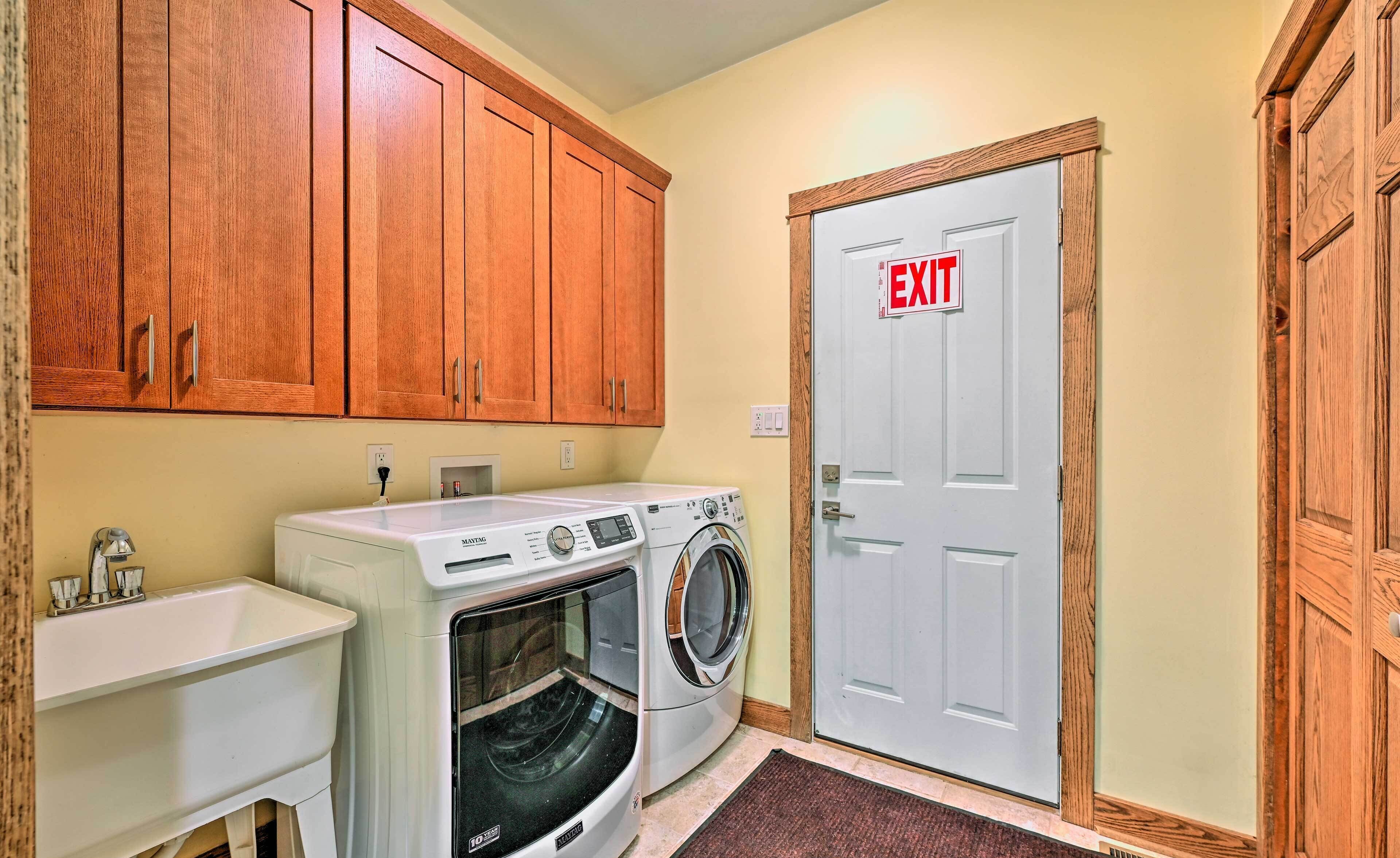 A laundry room with a washing machine, dryer, sink, and an exit door.