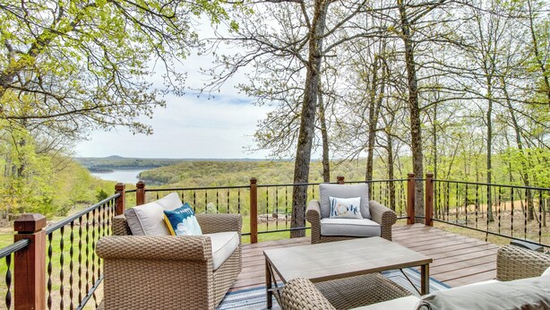 A deck with wicker furniture, a view of a lake, and a forested landscape. - Lake-view Retreat w/ Fire Pit in Mountain Home! (Mountain Home)
