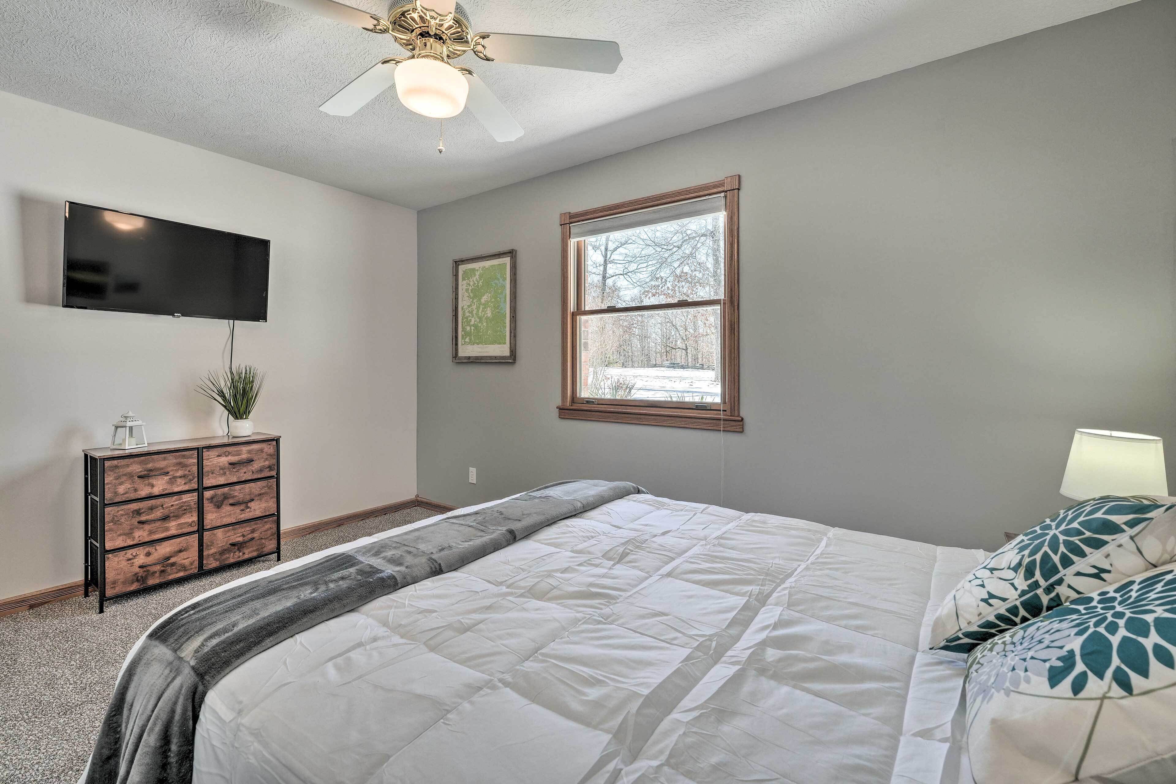 A bedroom with a bed, a ceiling fan, a TV mounted on the wall, a window, and a dresser.