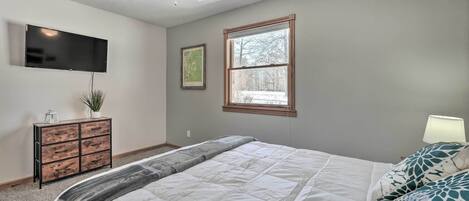 A bedroom with a bed, a ceiling fan, a TV mounted on the wall, a window, and a dresser.