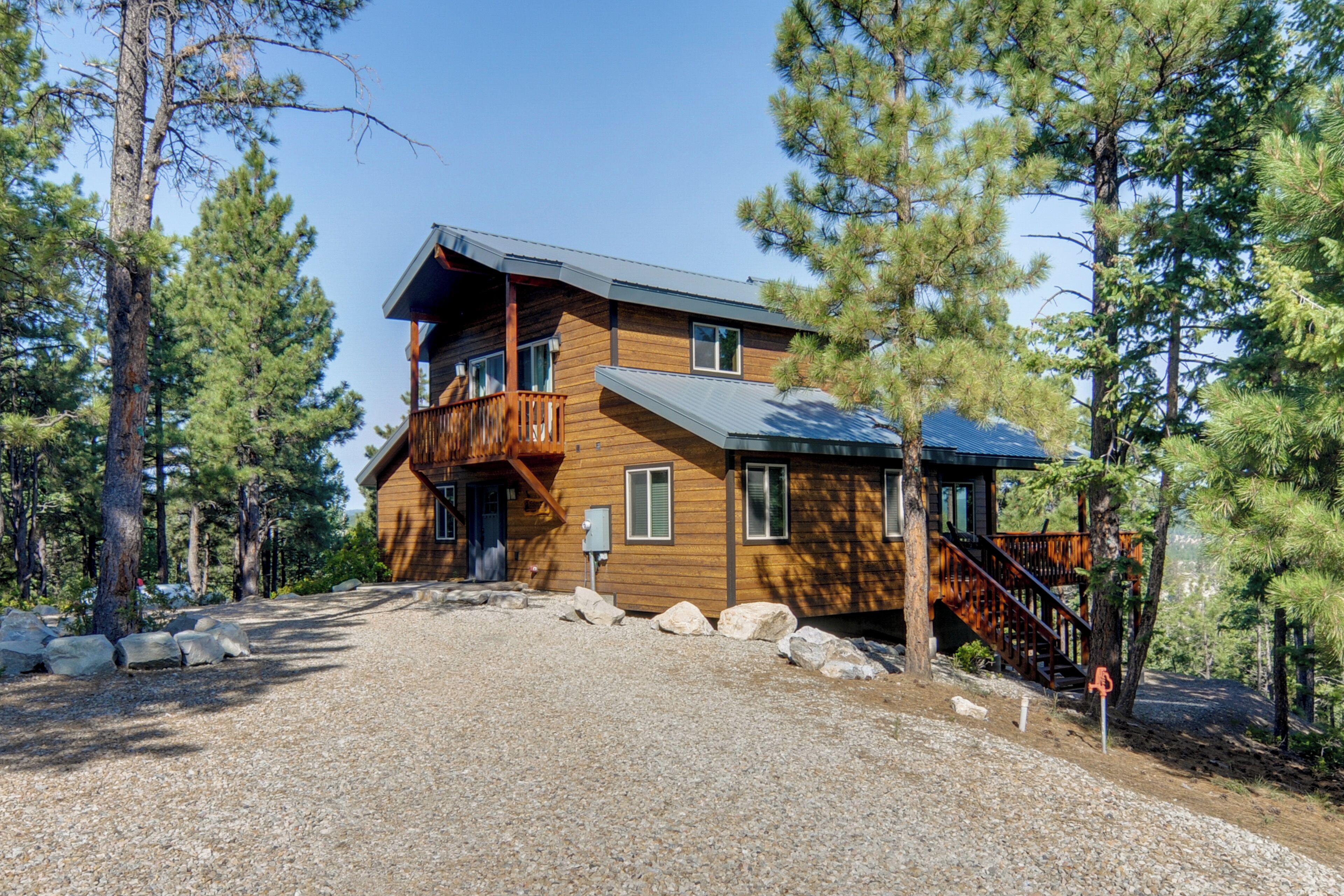 A two-story log cabin with a balcony, surrounded by pine trees.