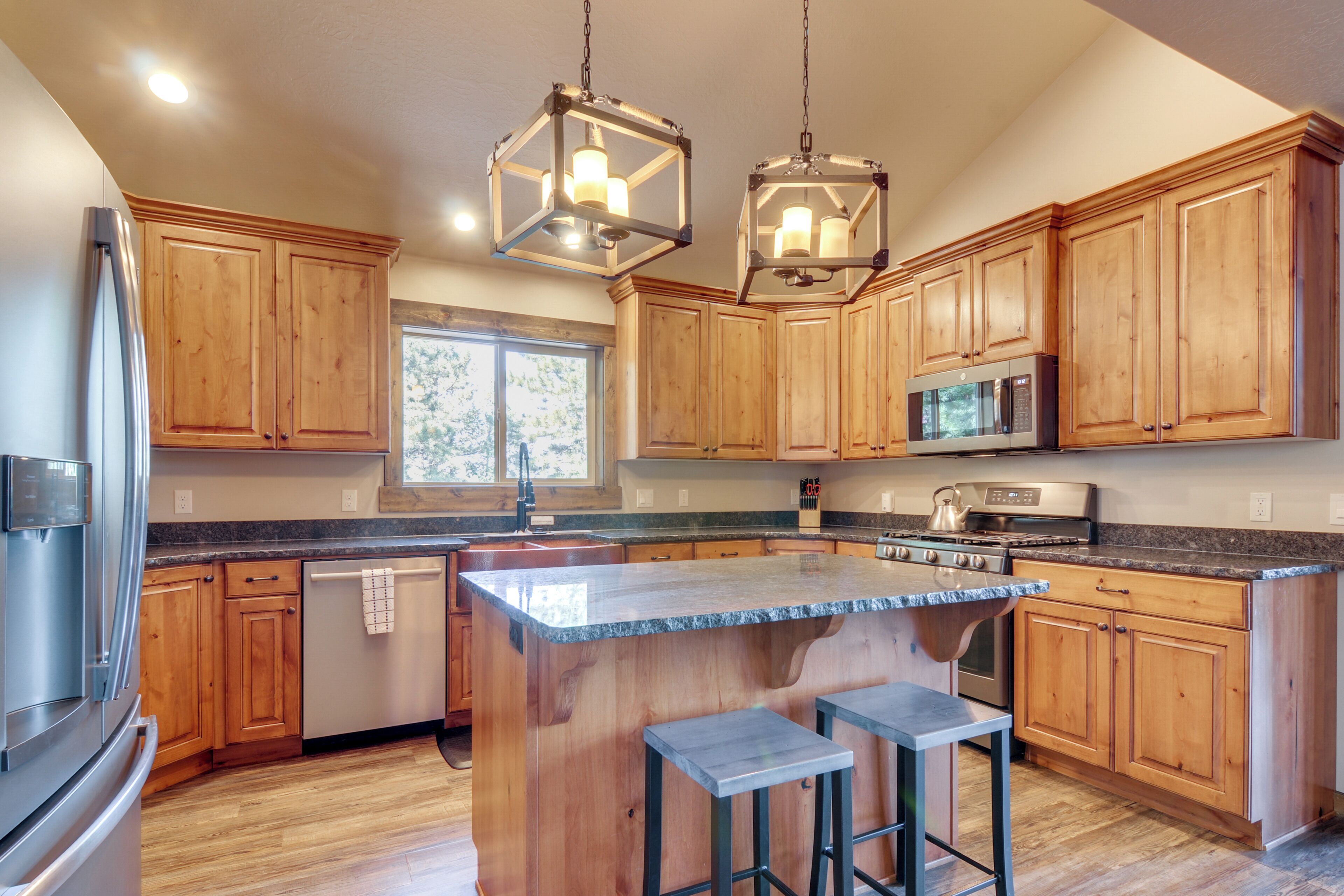 A modern kitchen with wooden cabinets, stainless steel appliances, and a central island with stools.