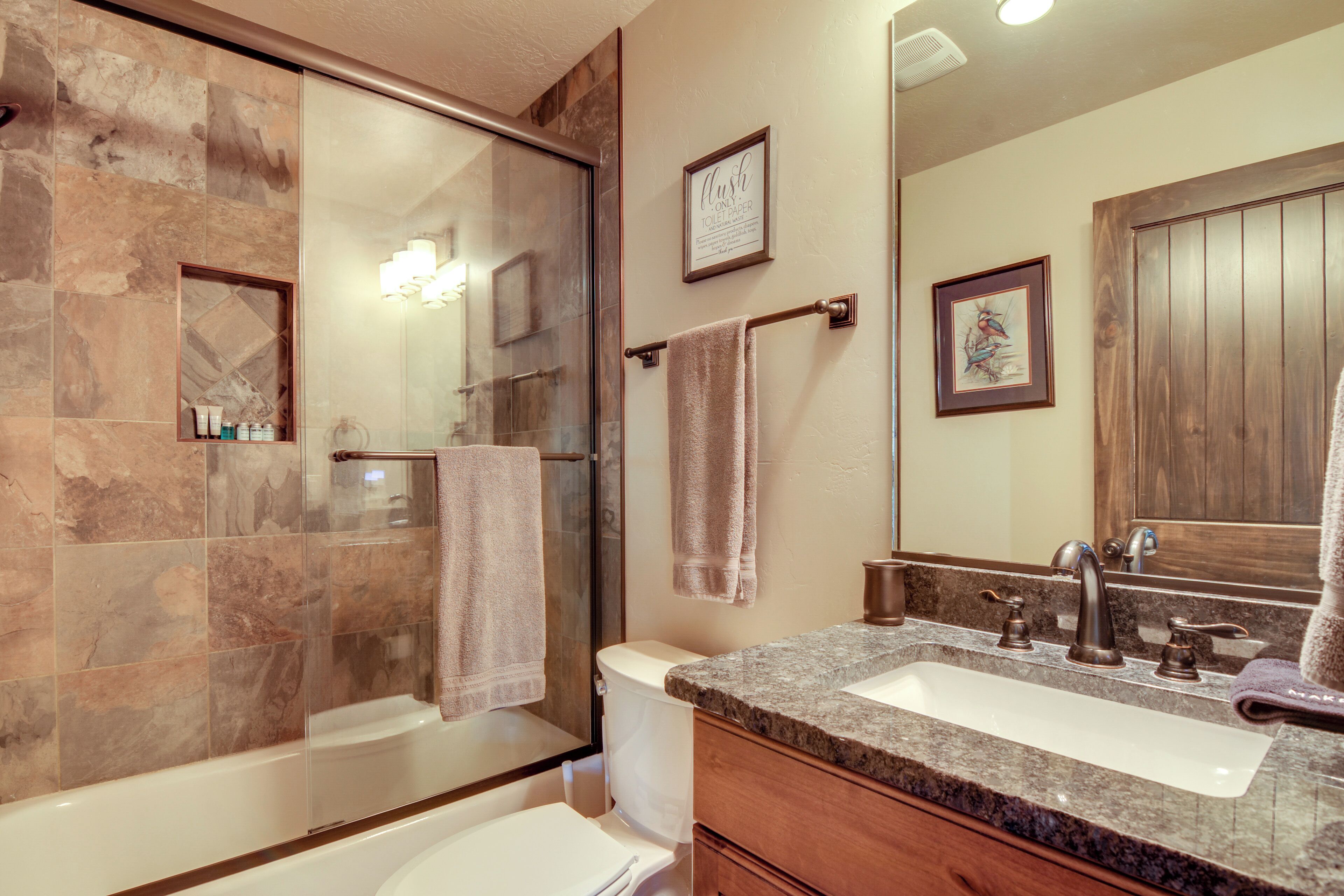 A bathroom with a glass shower enclosure, a white toilet, a sink with a wooden vanity, and a large mirror.