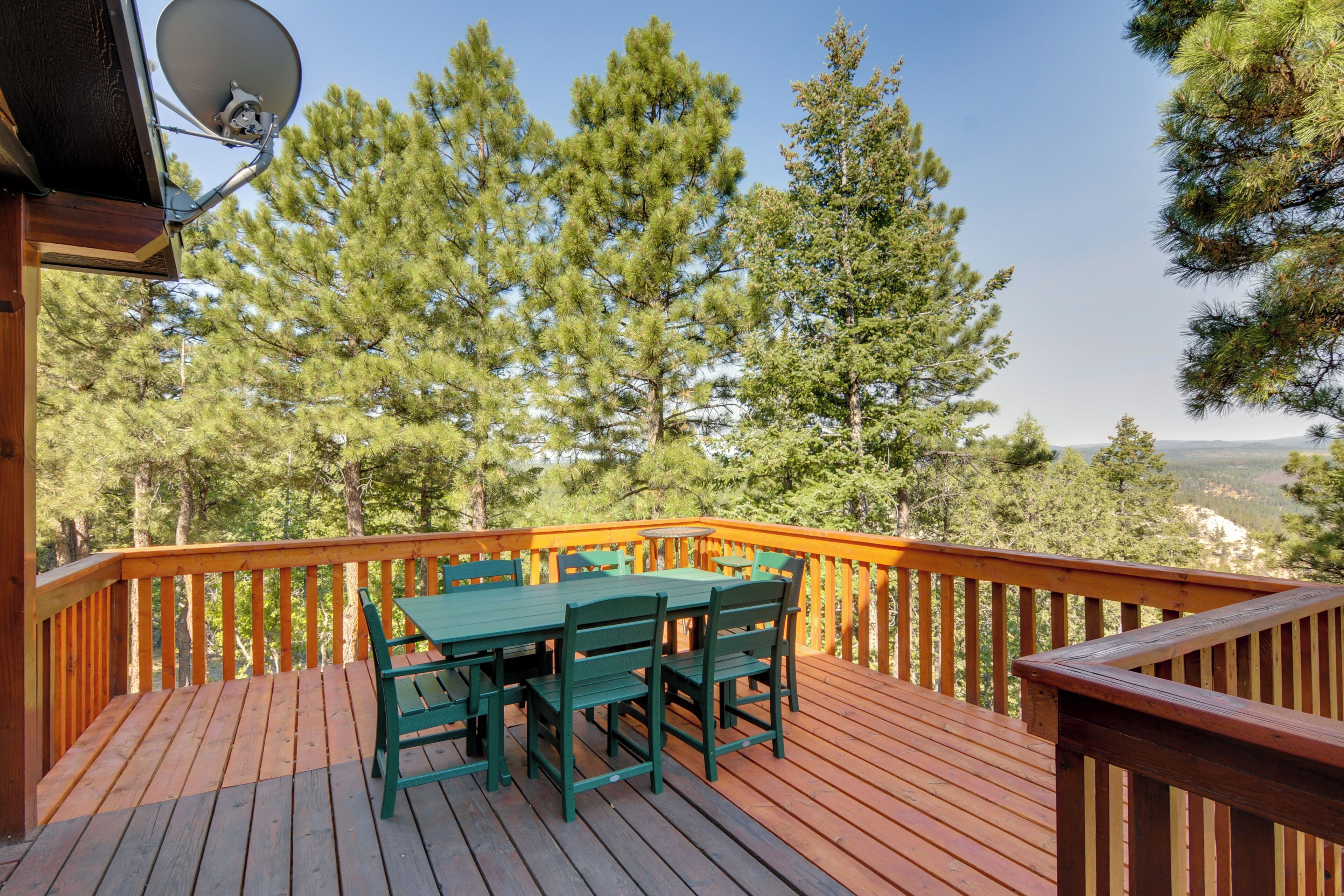 A wooden deck with a table and chairs, surrounded by a railing, overlooking a forested area.
