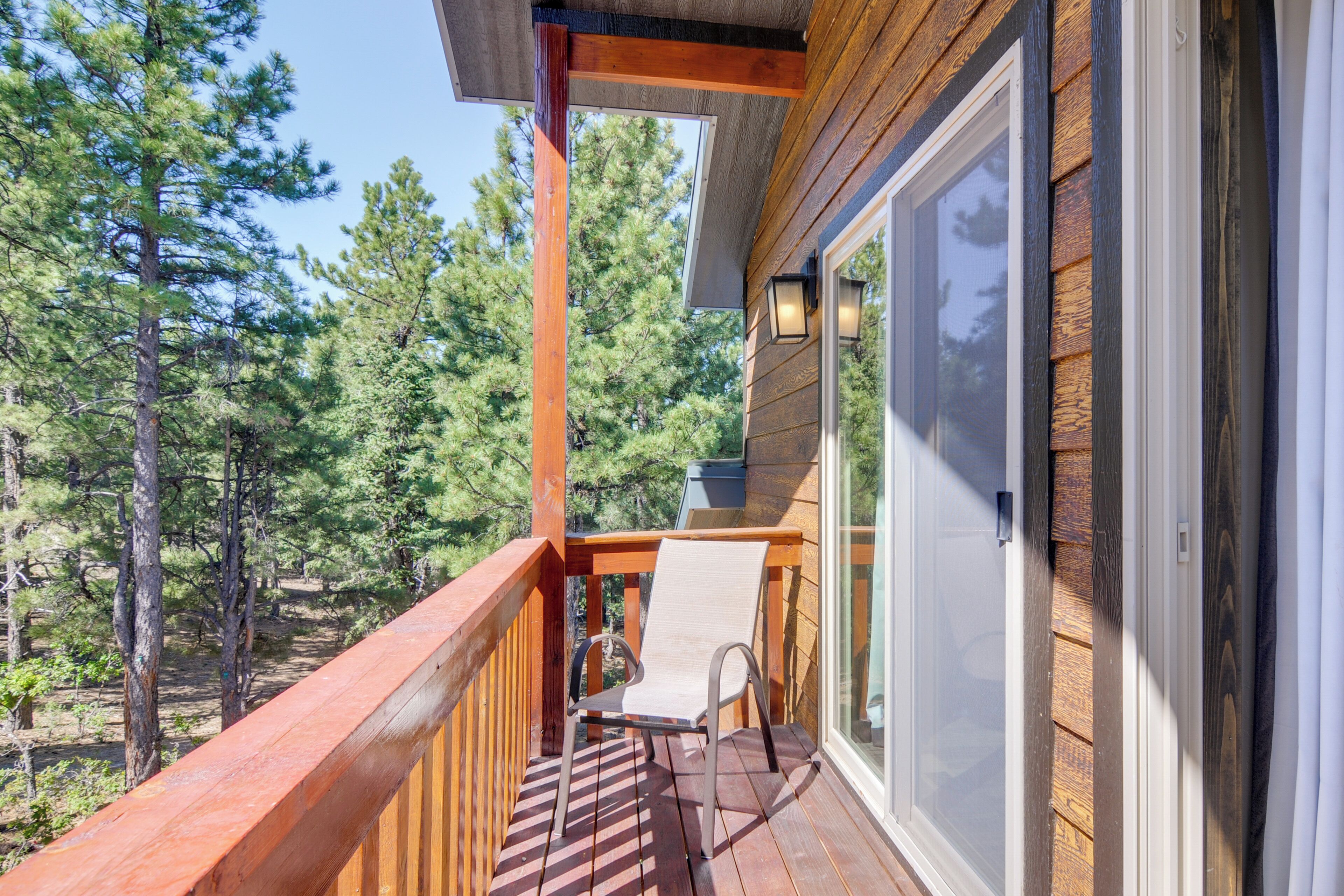 A wooden deck with a chair and a table, overlooking a forested area.