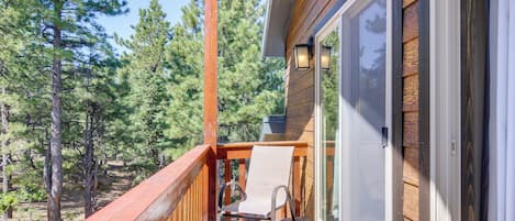 A wooden deck with a chair and a table, overlooking a forested area.