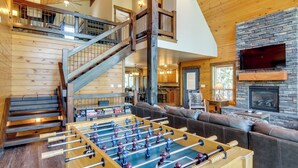 A spacious living area with a foosball table, a fireplace, a large TV, and a staircase leading to an upper level. - 'longview Lodge' w/ Furnished Deck & Fire Pit! (Duck Creek Village)