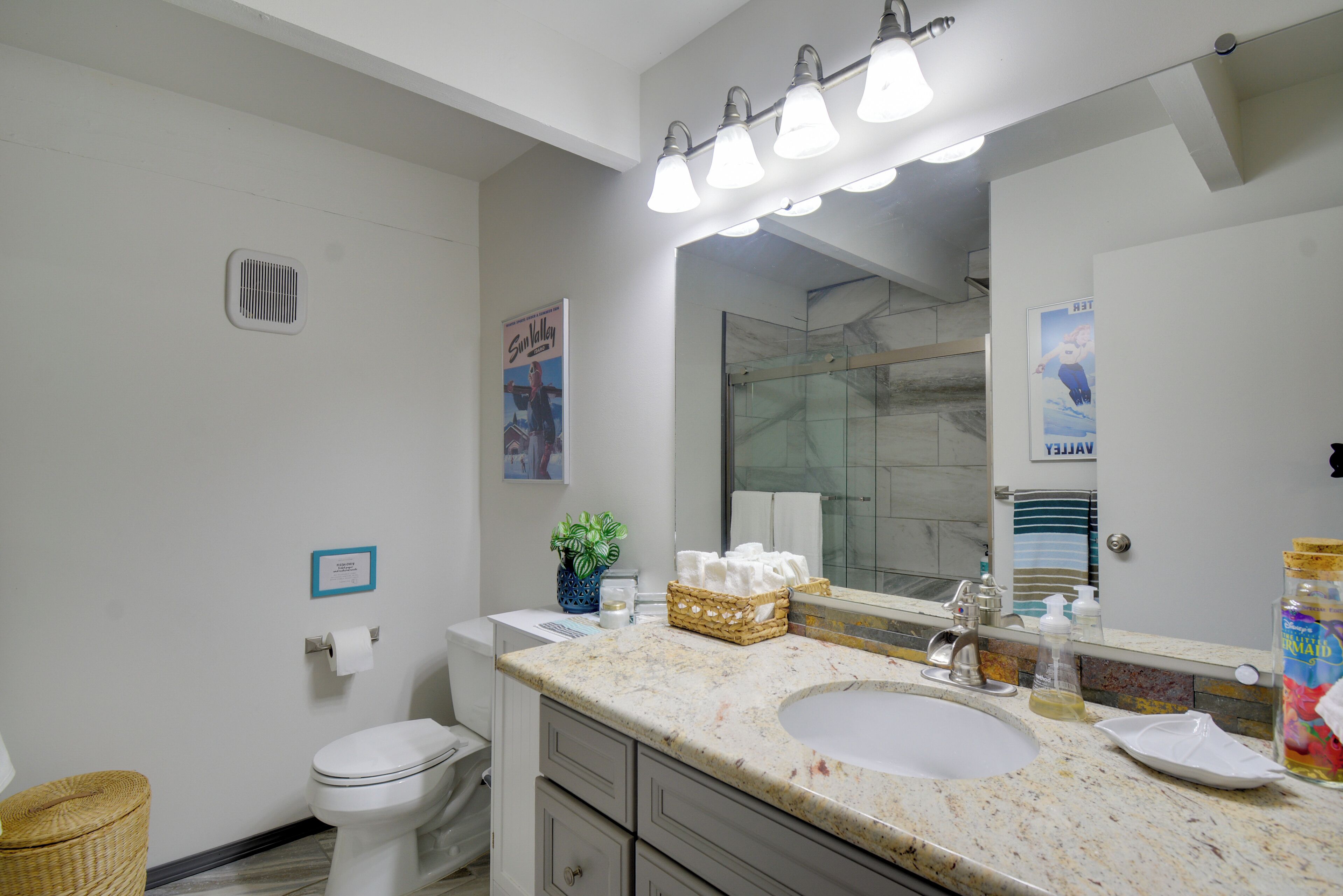 A bathroom with a sink, mirror, and toilet. There are towels and a basket on the counter.