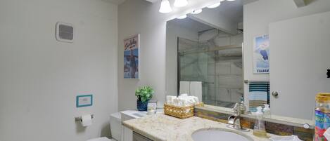 Une salle de bain avec un lavabo, un miroir et des toilettes. On y trouve des serviettes et un panier sur le comptoir.