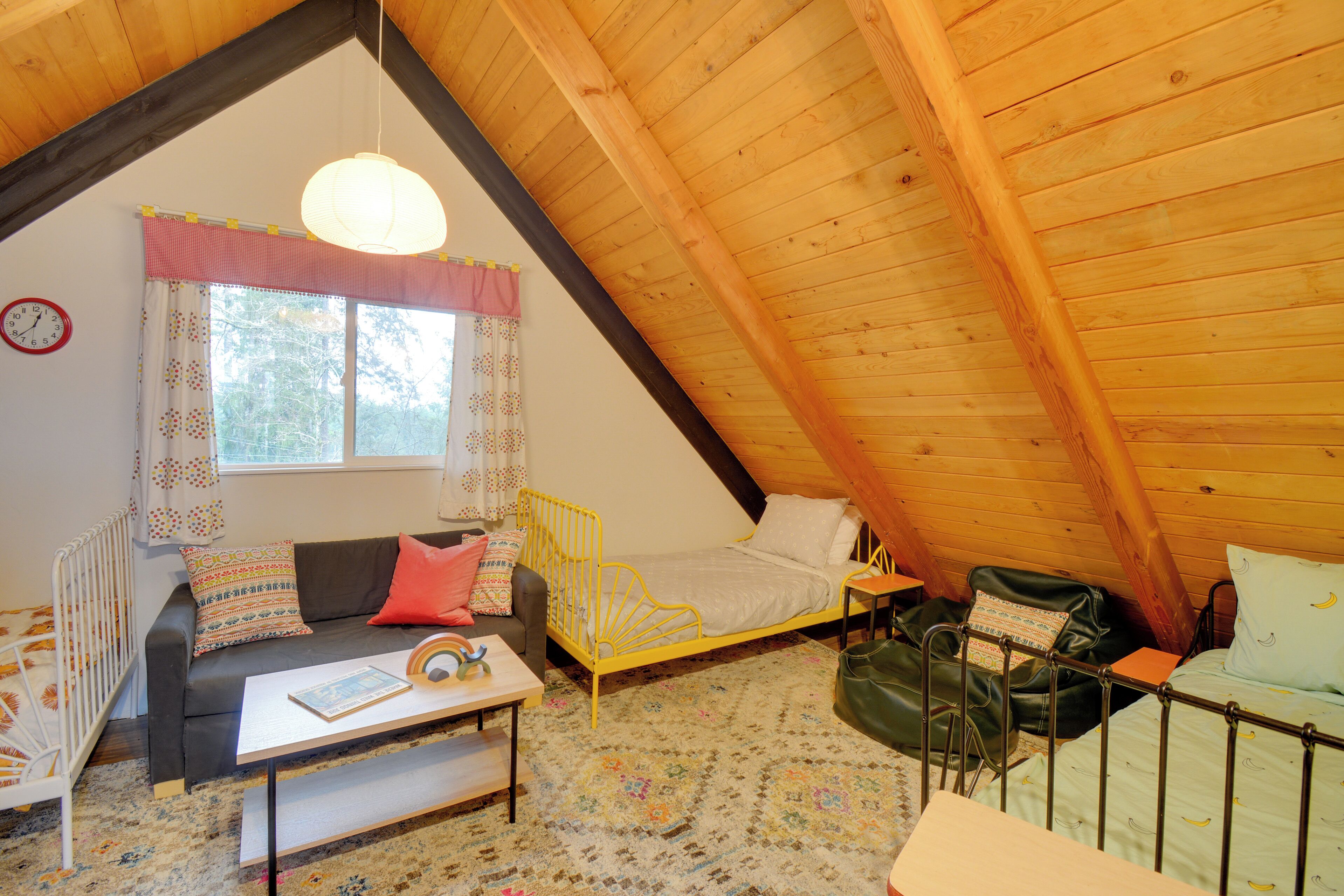 Ein gemütliches Schlafzimmer im Dachgeschoss mit schrägen Wänden, einem Bett, einer Couch, einem kleinen Tisch und einem Fenster mit Vorhängen.