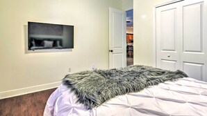 Un dormitorio con cama, televisor montado en la pared y una puerta que da a otra habitación.