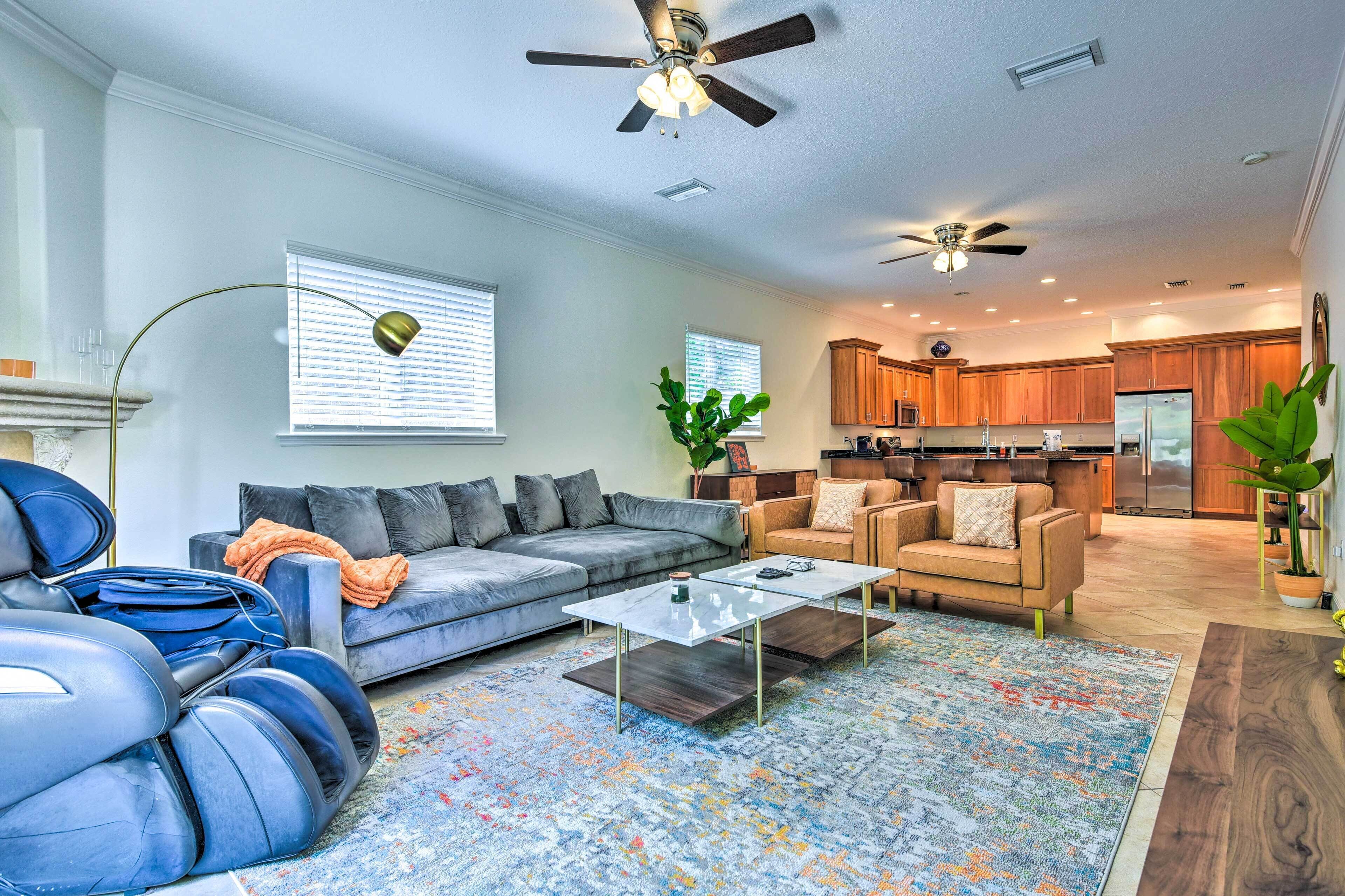 A spacious living room with a gray sectional sofa, a coffee table, and a blue massage chair.