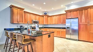 Una cocina moderna con armarios de madera, una isla central con taburetes de bar, electrodomésticos de acero inoxidable e iluminación empotrada en el techo.