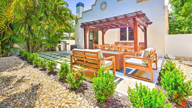 Un patio con una pérgola de madera, mobiliario exterior y un jardín con plantas pequeñas y guijarros.