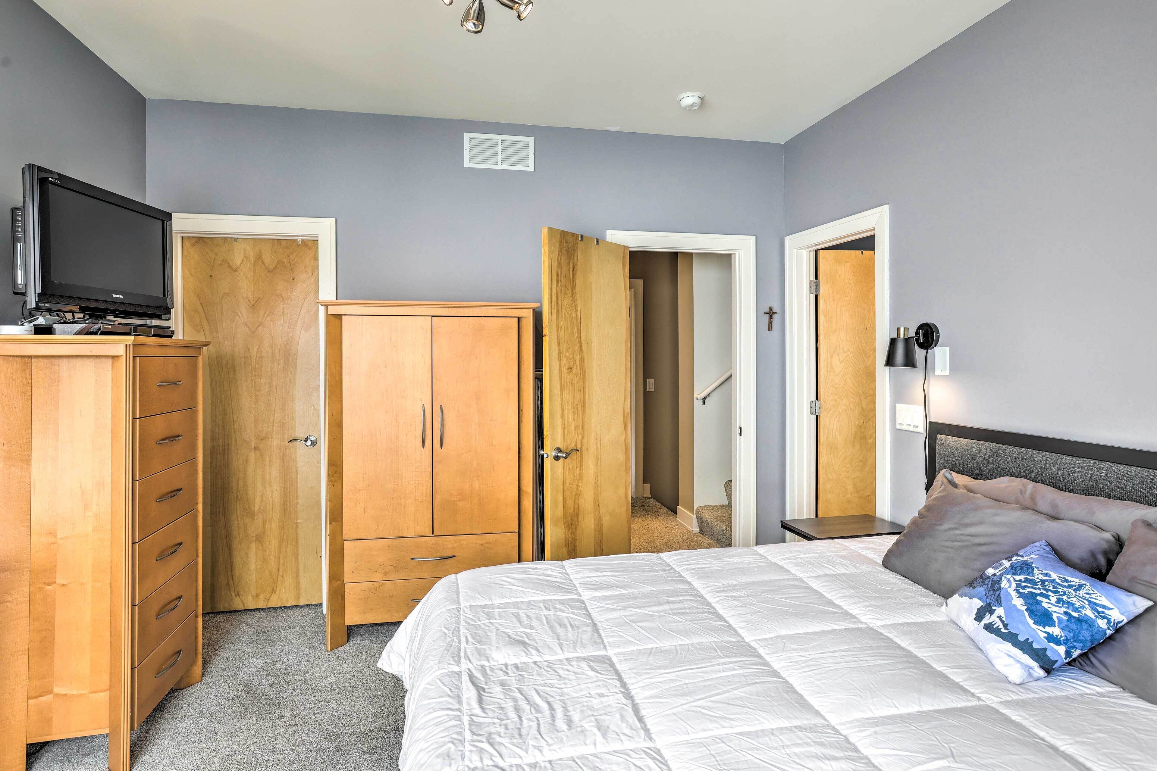 A bedroom with a bed, wooden wardrobe, and a television on a stand.
