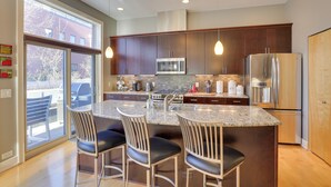 A modern kitchen with dark wood cabinets, stainless steel appliances, and a large island with bar stools. - Downtown Condo w/ Rooftop Patio & City Views! (Omaha)