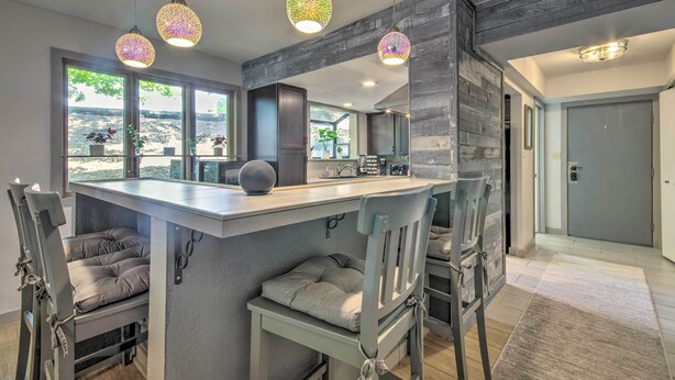 A modern kitchen with a central island, bar stools, pendant lighting, and large windows with a view. - 1 Mi to Lake of the Ozarks: Condo w/ Pool Access (Lake Ozark)