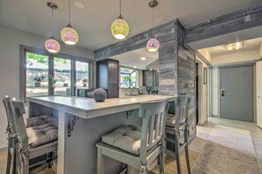 Una cocina moderna con una isla central, taburetes de bar, iluminación colgante y ventanas amplias con vistas.