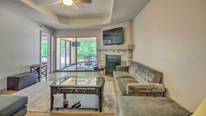 A spacious living room with a fireplace, a ceiling fan, and a large TV mounted on the wall. - 1 Mi to Lake of the Ozarks: Condo w/ Pool Access (Lake Ozark)
