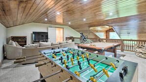 A spacious living area with a foosball table, a pool table, a sofa, and a television.