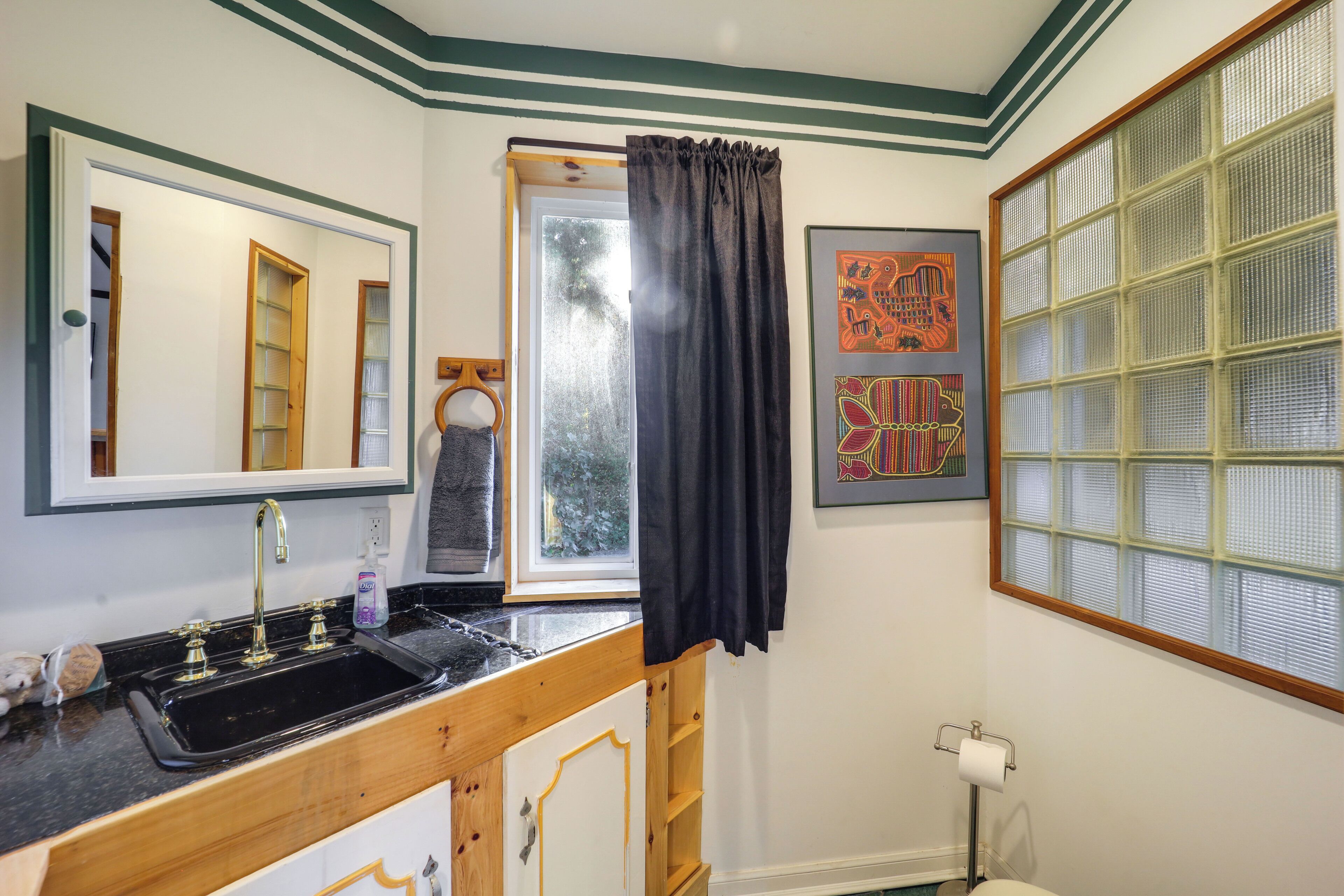 A bathroom with a black sink, wooden vanity, and a window with a curtain.