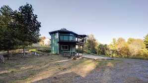 A two-story house with a balcony, surrounded by trees and a gravel driveway. - Unique West Jefferson Home w/ Fire Pit & Grill! (West Jefferson)