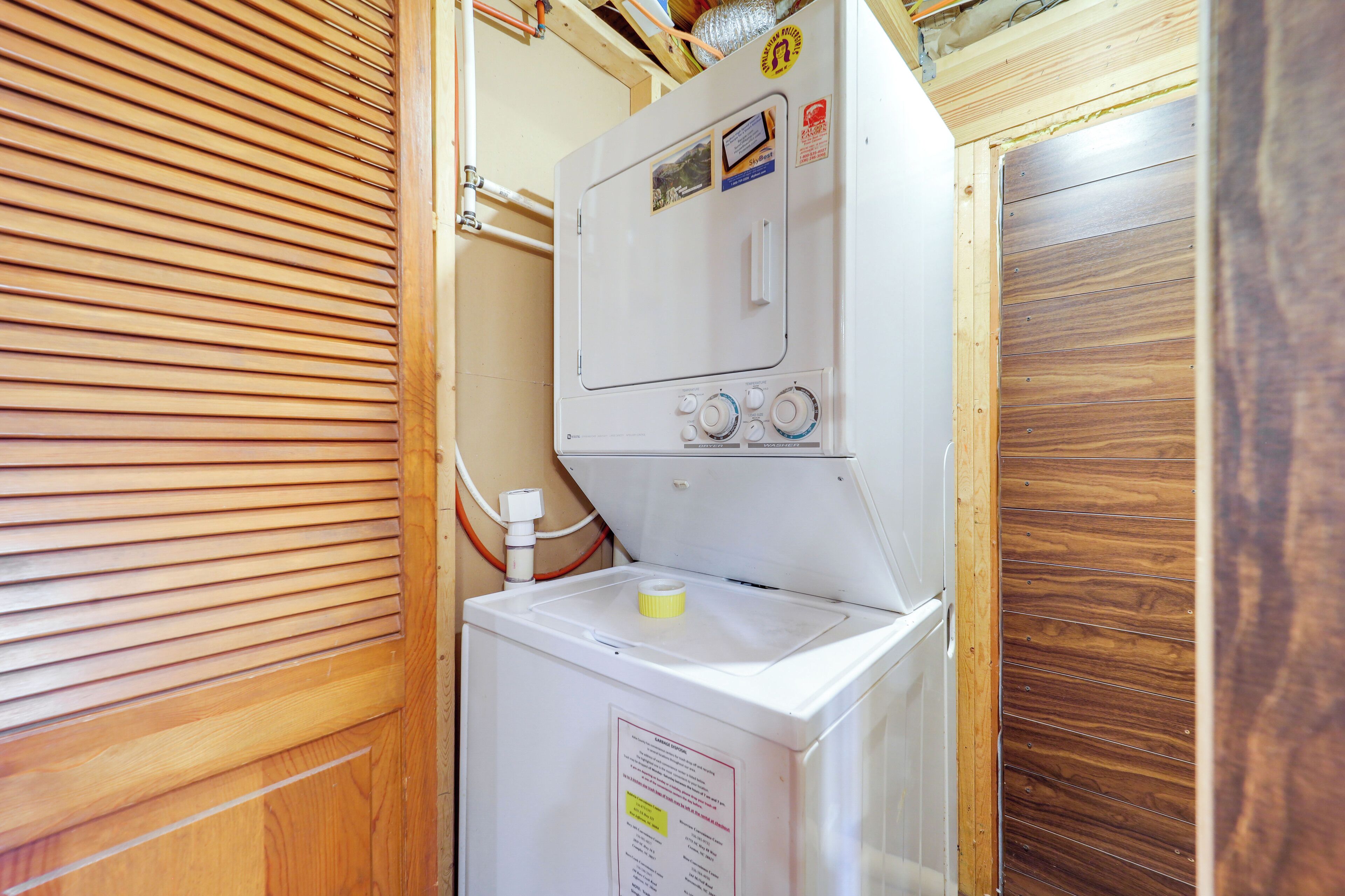 A compact laundry area with a washing machine and dryer, wooden paneling, and visible plumbing.